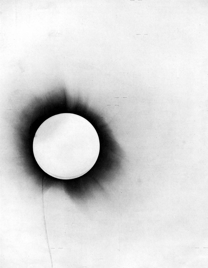 A historical negative of the 1919 total solar eclipse, with a bright disk and dark corona against a pale field.